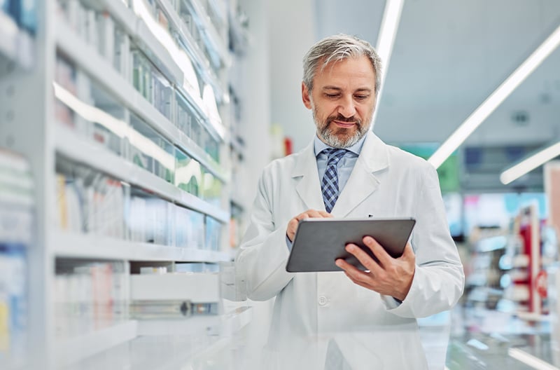 Pharmacist reviewing license records on a tablet in the pharmacy